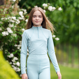 Girl walks in garden wearing the LeMieux Young Riders Base Layer in aqua with matching riding tights