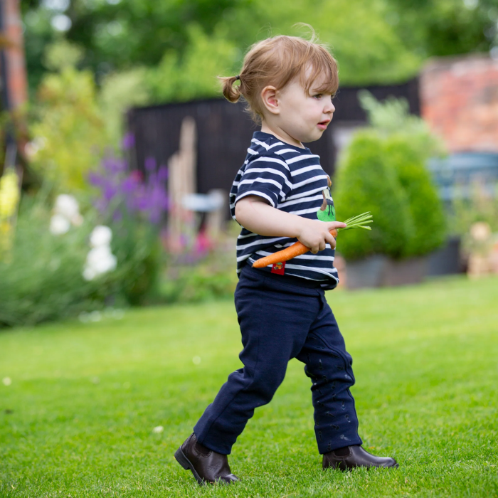 Little girl walks with a carrot for her pony wearing the Shires Childrens Winnie & Me Jodhpurs in Navy