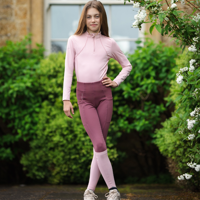 Girl rider stands outdoors wearing the LeMieux Young Rider Orla Pull Ons in rosewood