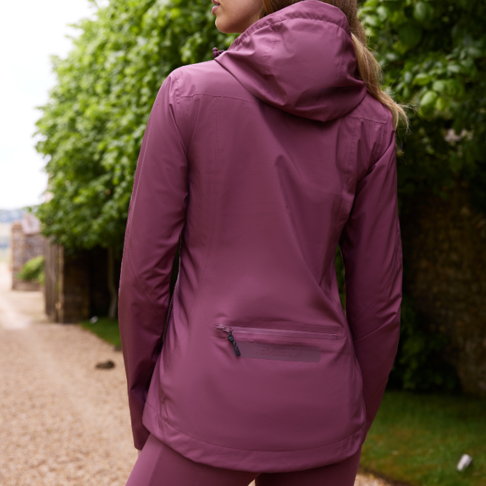 Female turns to show the reverse detail on the LeMieux Isla Short Waterproof Jacket in Rosewood