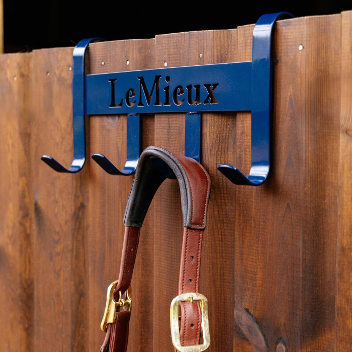 The LeMieux Headcollar Hanger in navy hooked over a stable door with a brown headcollar hanging from one of the rails