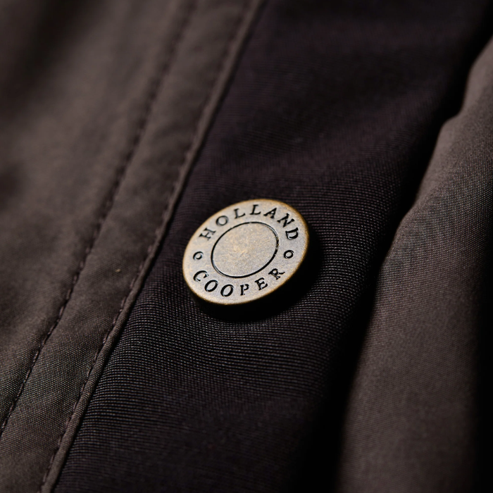 Logo button detail in antique brass on the Holland Cooper Stamford Country Coat in Chocolate