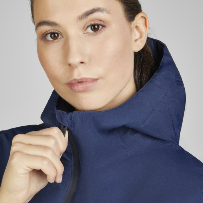 Woman demonstrating the zip fastening for Eskadron Heritage Waterproof Jacket in true blue