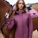 Female stands with a horse wearing the LeMieux Isla Short Waterproof Jacket in Rosewood