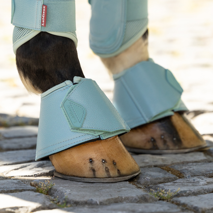 Horses hooves with the LeMieux Arika Over Reach Boots in aqua