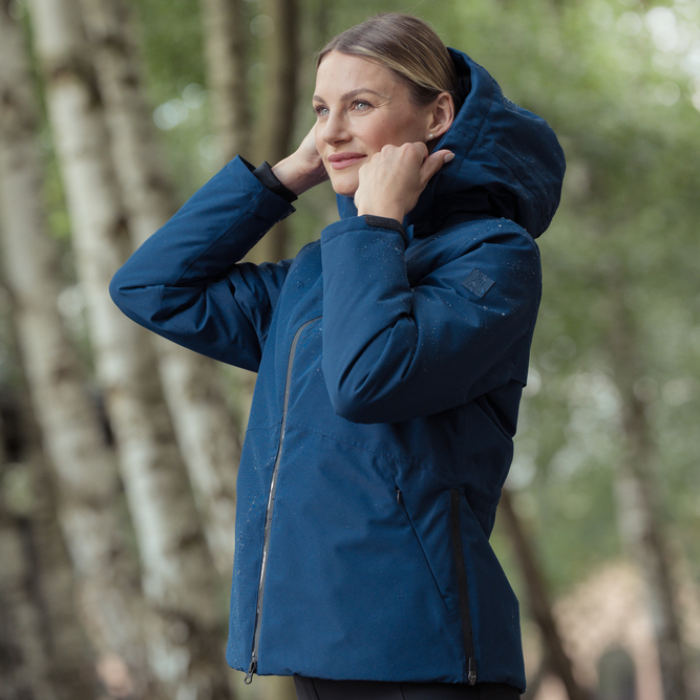 Woman outdoors amongst trees wearing the Eskadron Heritage Waterproof Jacket in true blue