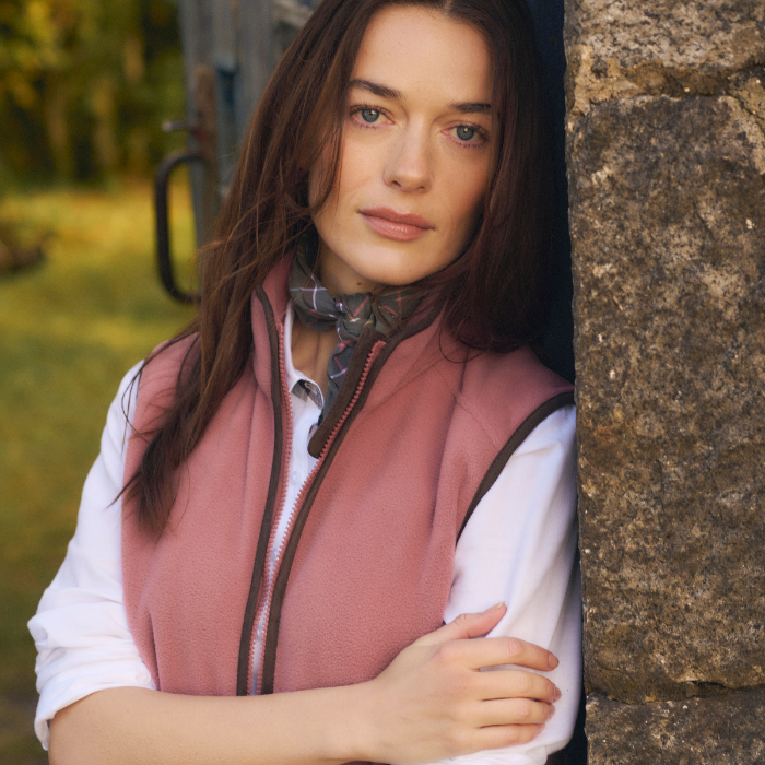 Female leans up against a tree wearing a crisp white shirt and silk neck scarf, layered over with the Ladies Country Colton Fleece Gilet in Deep Pruce