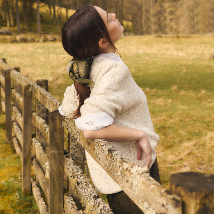 Woman rests against a fence in 
the countryside wearing the Barbour Edda Knitted Jumped