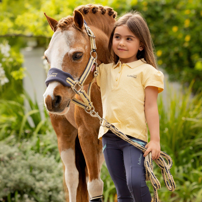 Girl stands by pony wearing LeMieux Mini Polo Shirt in Mimosa